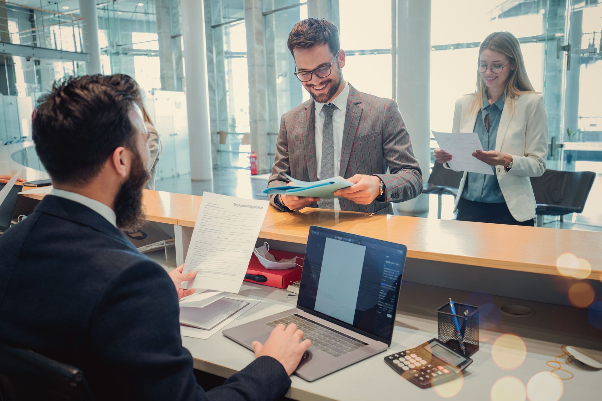 Group of employees working together at a desk with laptops in an office.