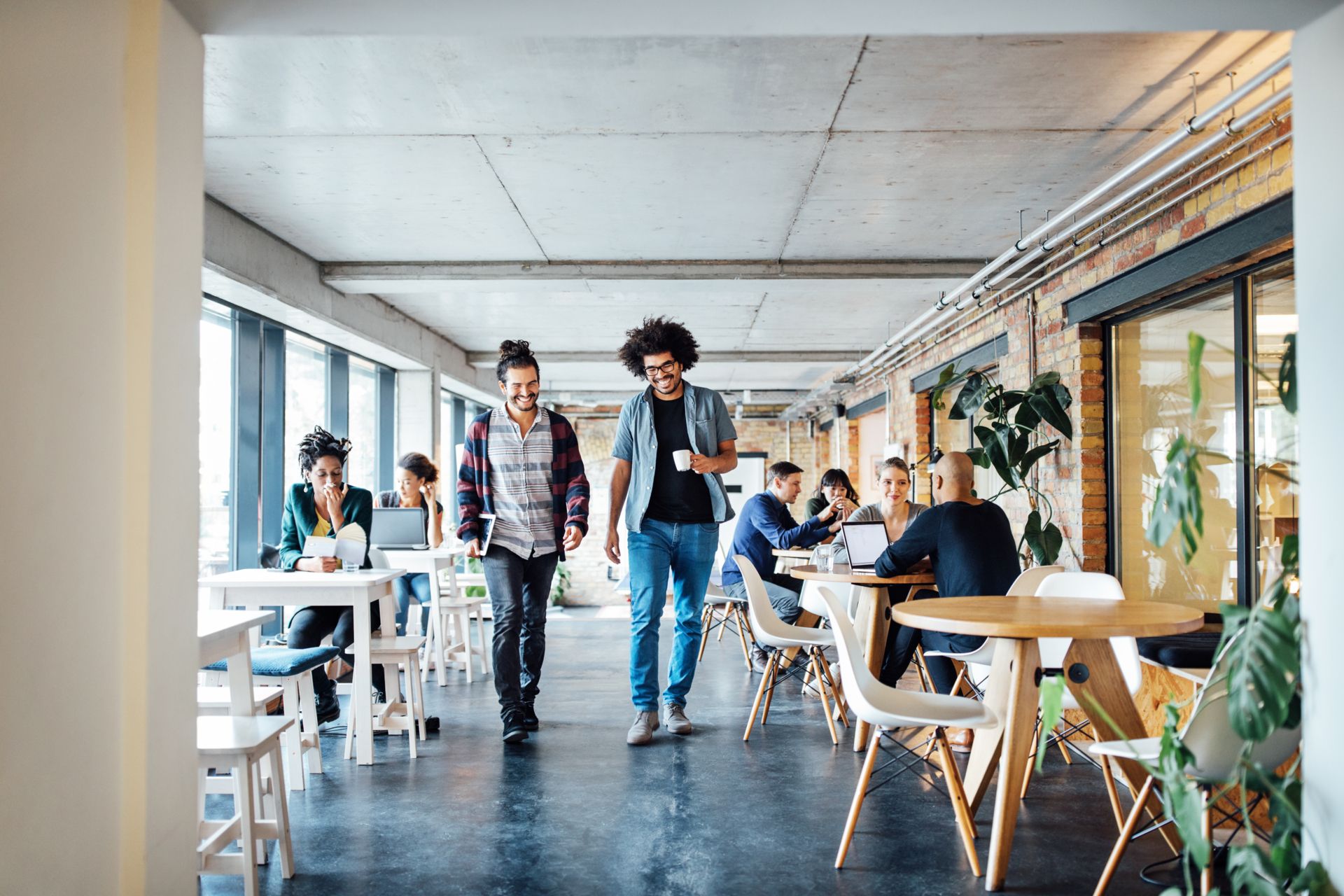 Group of people walking in a room with tables and chairs.